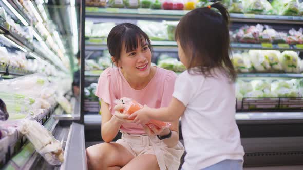 Asian young beautiful mother holding grocery basket with her little kid child walking in supermarket