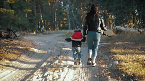 Young Mother Walking with a Little Son in Autumn Forest.
