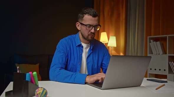 Smiling Satisfied Young Bearded Businessman in Eyeglasses Sitting in Front of Camera at Home Office