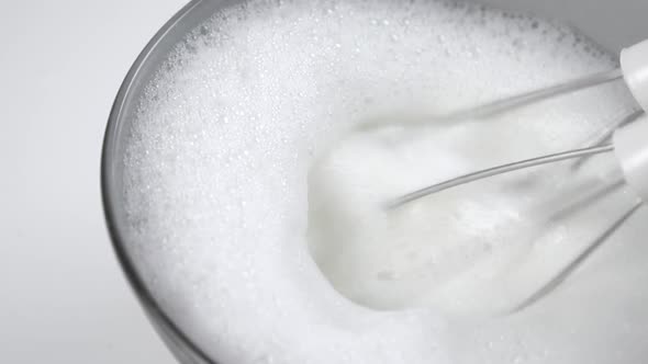 Mixer whips milk in slow motion. Rotating beaters and foam with bubbles in a gray bowl