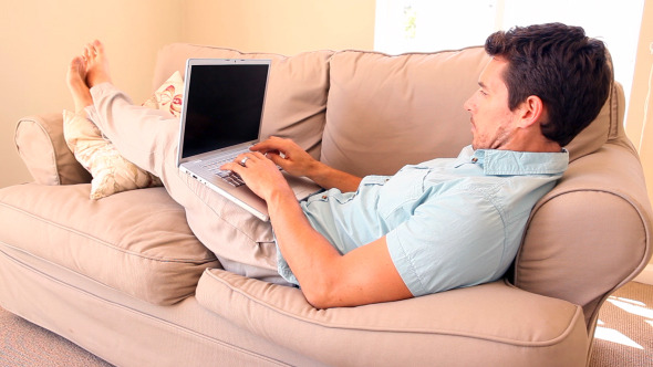 Man Lying On Couch Typing On Laptop