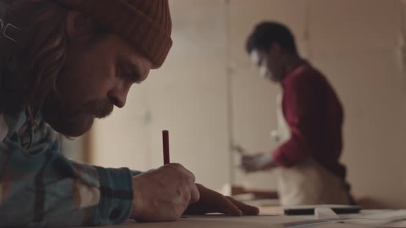 Caucasian Craftsman Drawing on Piece of Wood in Workshop