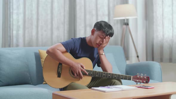 Asian Boy Composer With A Guitar Having A Headache While Composing Music At Home