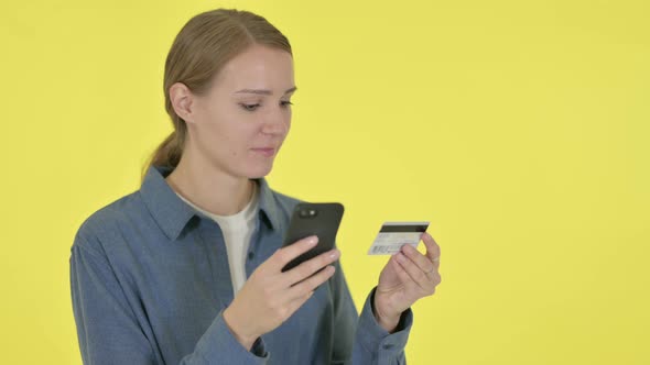 Young Woman with Successful Online Shopping on Smartphone on Yellow Background