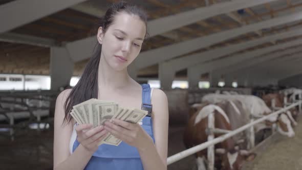 Portrait of Young Cute Female Farmer Worker on the Cow Farm Counting Cash