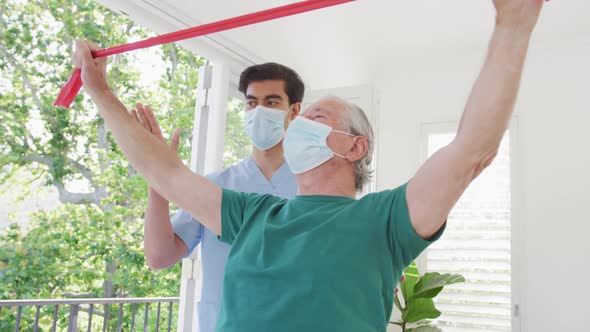 Male therapist and senior man wearing face masks while exercising at nursing home during covid