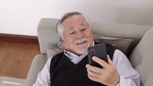 An Asian Elderly video call with smartphone on the sofa on a relaxing day.