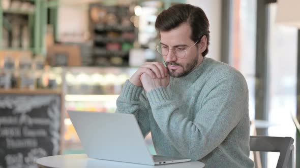 Young Man with Laptop Thinking in Cafe