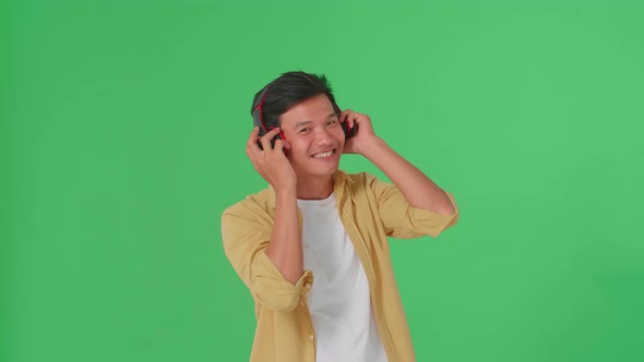 Asian Man Listening To Music With Headphones And Dancing In The Green Screen Studio