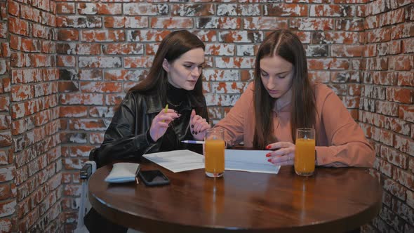 Two Girls are Working in a Cafe with Documents