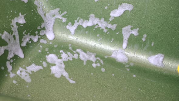 Hand in Yellow Glove Using White Foam Detergent Spray Into Green Glittering Bath