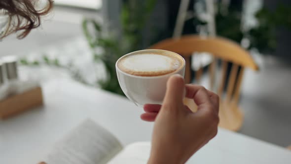 Office Worker Girl Sits At Lunch In A Restaurant Drinking Fresh Hot Cappuccino While Reading A Book