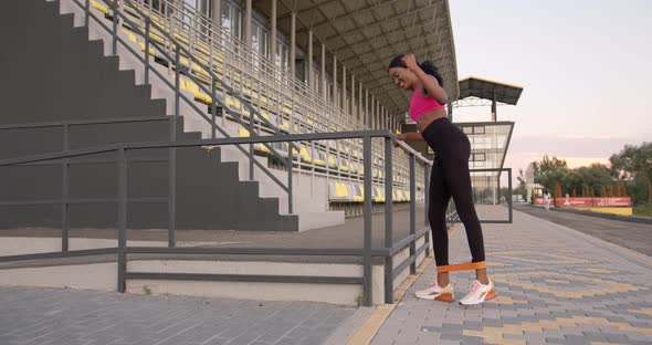 Happy Motivated Black Woman Doing Exercises for Legs with Rubber Stripe