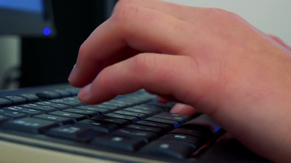 A Woman Sits at a Desk in Front of a Computer Screen and Types on a Keyboard - Closeup on the Hands