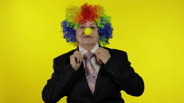 Senior Elderly Clown Businesswoman Boss in Wig Adjusts Tie. Yellow Background