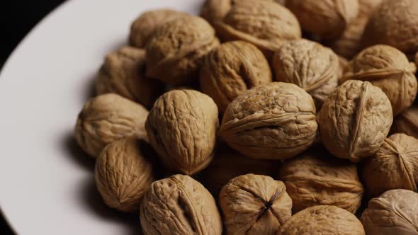 Cinematic, rotating shot of walnuts in their shells on a white surface