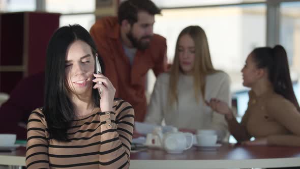 Young Serious Caucasian Woman Talking on the Phone While Her Friends Chatting at the Background in