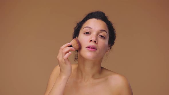 Beauty Portrait of Young African American Woman Applying Powder to Her Face Using Makeup Brush