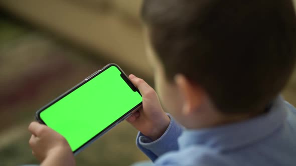 Back View of Boy Holding Phone with Chroma Key Green Screen and Watching Content