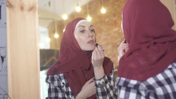 Young Muslim Woman in a Hijab in Front of a Mirror Paints Her Lips