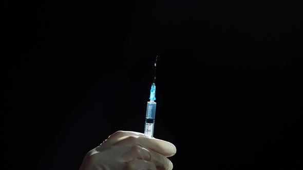 Hand in Protective Medical Gloves Holding Syringe on Black Background