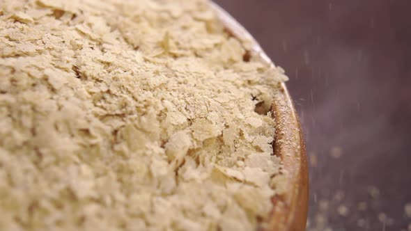 Nutritional brewers yeast flakes falling on a full rustic wooden bowl in slow motion. Macro