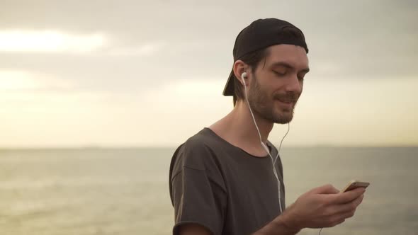 Closeup Smiling Caucasian Bearded Man with Cap on Backward Listening Music Using Headphones Early in