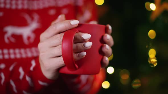 Unrecognizable Woman Holding Cozy Red Mug on Glowing Christmas Tree Background