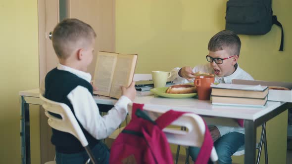 Smiling Boy Holds Textbook and Friend Eats Pizza at Table