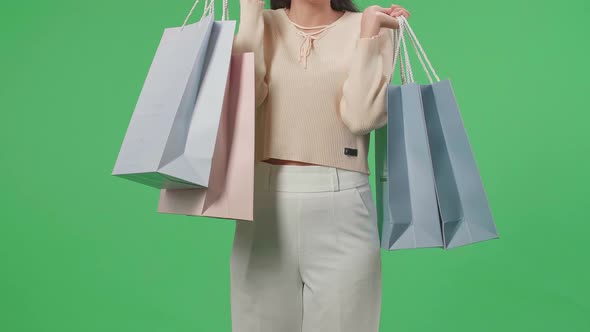 Front View Of Woman Holding Shopping Bags Up Before Posing And Smiling In Front Of Green Screen