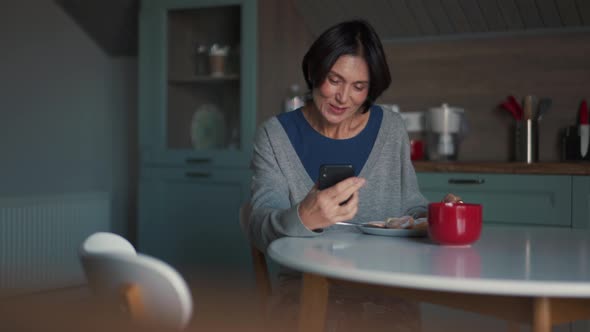 Smiling woman eating food and talking by video call on phone