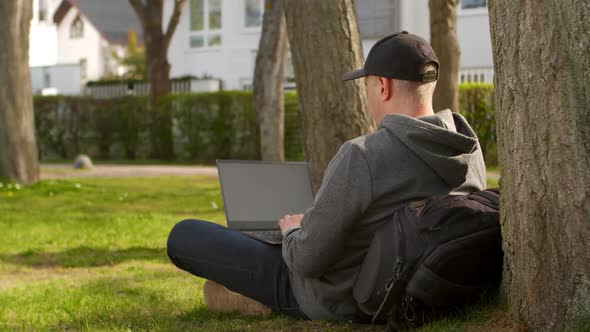 Young Man is Sitting in a Park in a Tourist Place Working on a Laptop
