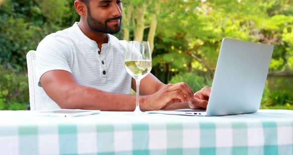 Smiling man using laptop while having wine in garden 4k