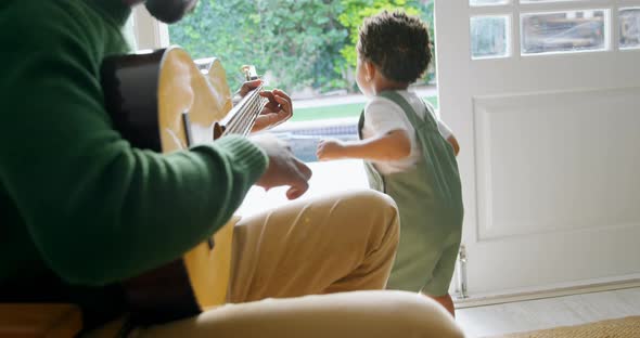 Side view of young black father playing guitar and sitting on chair in a comfortable home 4k
