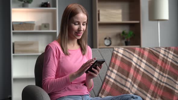 Calm ginger concentrated woman using modern smartphone while spending time at home