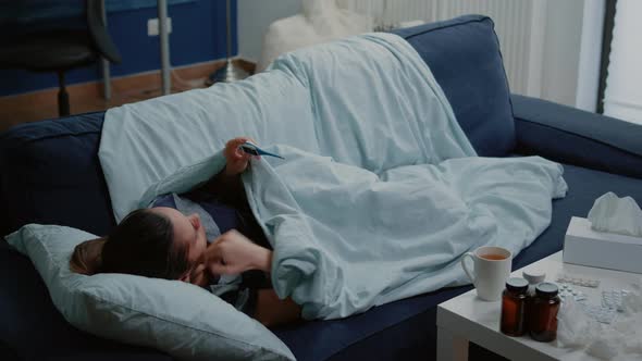 Woman with Disease Laying on Couch and Measuring Fever