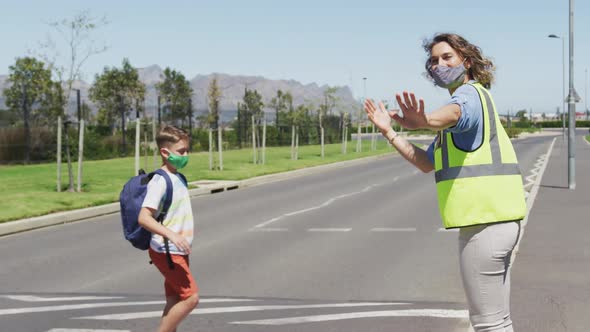 Caucasian female teacher wearing a face mask and high visibility vest stopping traffic on a pedestrian