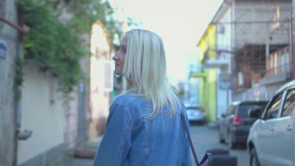 Rear view of young stylish blonde in denim jacket walking through city center