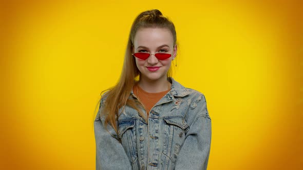 Sincere Cool Cheerful Stylish Girl in Denim Jacket Wearing Sunglasses Charming Smile on Yellow Wall