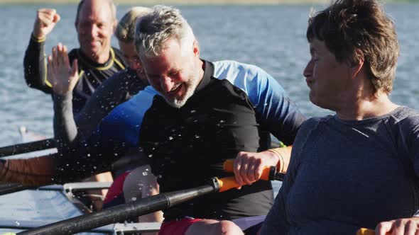 Four senior caucasian men and women in rowing boat raising hands and cheering