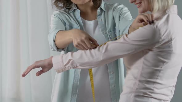 Smiling Designer Measuring Female Customer Arm, Discussing the Dress Order