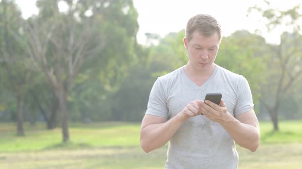 Happy Young Man Smiling While Using Phone at the Park