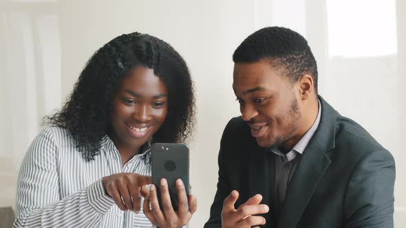 Amazed Happy African Businesswoman Demonstrating Smartphone Screen to Young Male Colleague