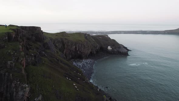 AERIAL: Fly along coastal cliffs towards abandoned boathouse, Rhossili Gower, 4k Drone