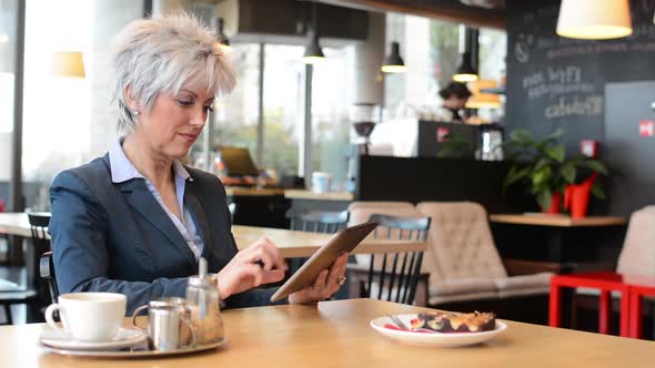 Business Middle Aged Woman Works on Tablet in Cafe - Coffee and Cake