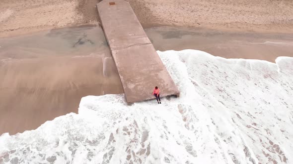 Woman relaxes by sea sitting on edge of pier and swing feet near water surface