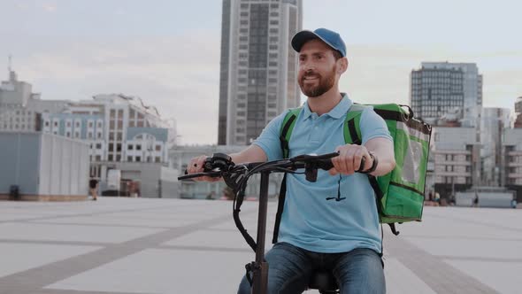 Man Courier Food Delivery with Thermal Backpack Rides the Street on an Electric Scooter Deliver