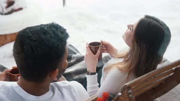 Happy Young Couple Drinking Hot Chocolate While Sitting on the Bench Outdoors on Winter Day