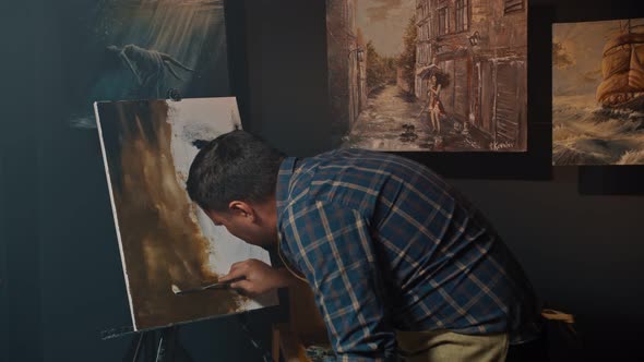 Artist Man is Sitting on a Stool at Home in Front of Canvas and Working with Inspiration Drawing a