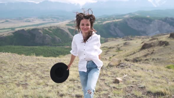 Attractive Brunette in a Hat and White Shirt Is Enjoying Nature in the Mountains. Beautiful Young